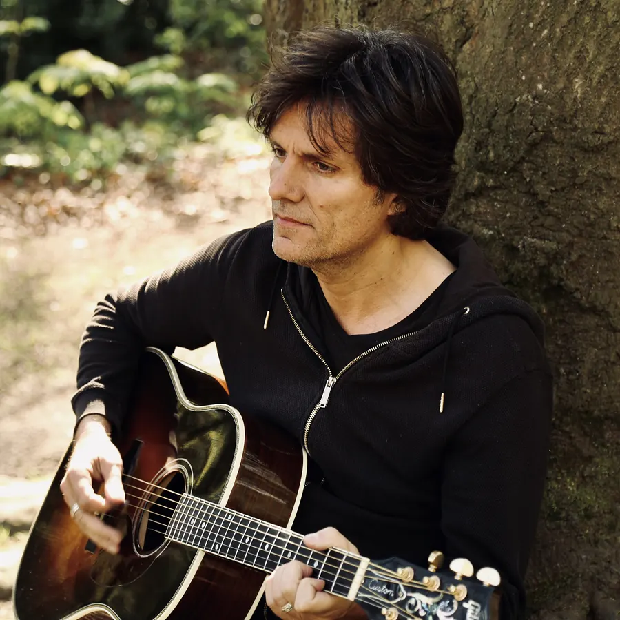 Lionel Fornetti with an acoustic guitar against a tree