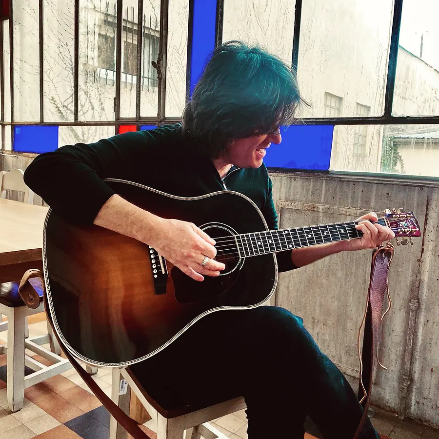 Lionel Fornetti playing an acoustic guitar by a window