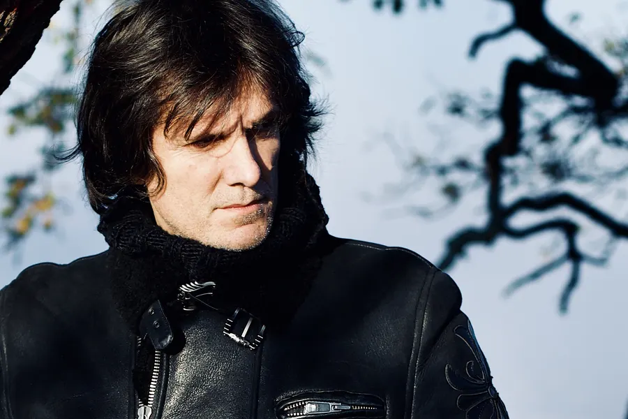 Close portrait of Lionel Fornetti in a leather jacket, branches against the sky
