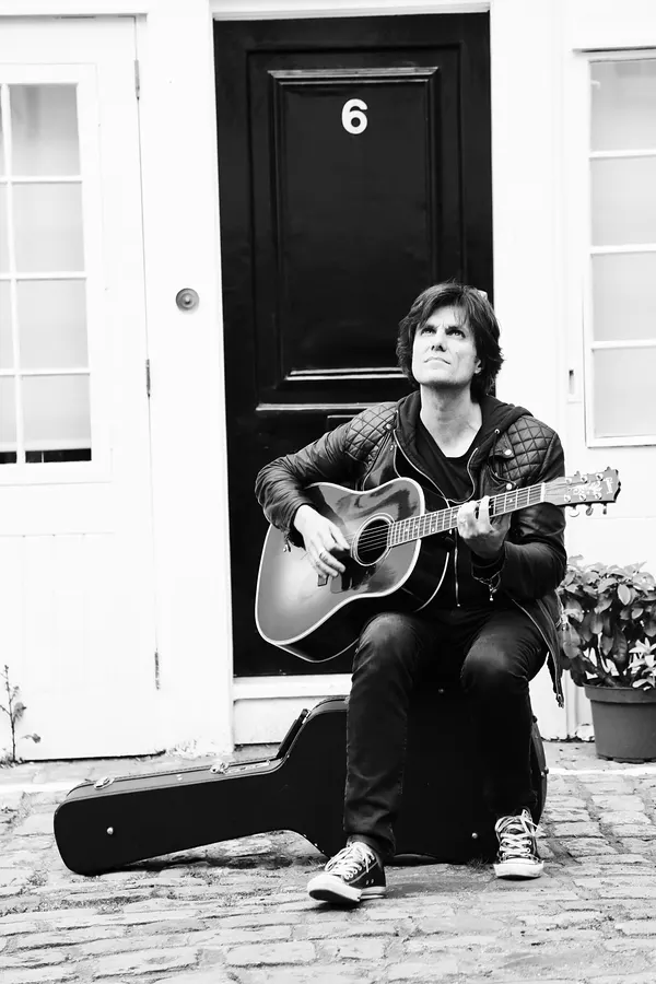 Lionel Fornetti sitting on a doorstep with his guitar, black and white