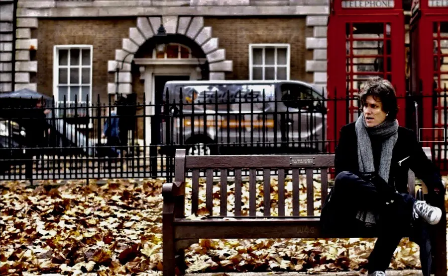Lionel Fornetti on a bench among autumn leaves, red phone box behind