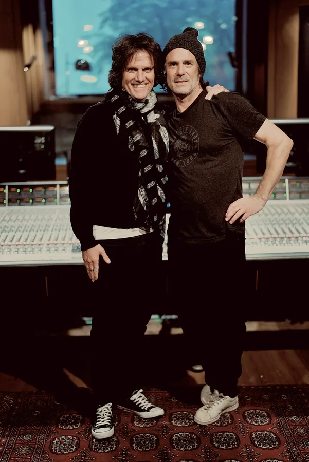 Two men posing in front of a studio mixing console